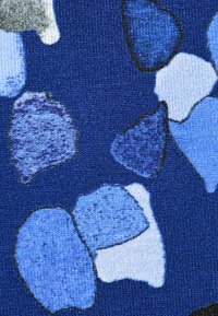 Blaues Textil mit ungewöhnlichen Formen in verschiedenen Blau-, Weiß- und Grautönen, die von Schwarz umrandet sind, wodurch ein geschichtetes Muster entsteht.