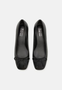 Ballerines véganes noires avec un bout rond, une semelle plate, une texture lisse et un accent en forme de nœud à l'avant. À l'intérieur, on trouve une semelle intérieure étiquetée.