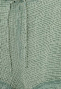 Tissu vert clair texturé avec des cordons verticaux et une apparence légèrement froissée, montrant les détails des coutures et de l'ourlet.