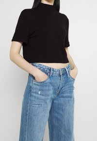 Svart kortärmad t-shirt med rullade ärmar och hög halsringning, matchad med ljusblå slitna vida jeans med framfickor.