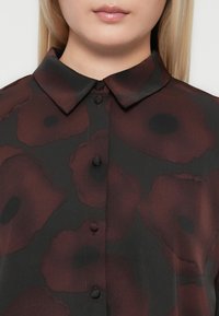 Svart skjorte med maroon blomsterdesign, med spiss krage og knappelukking, laget av et glatt, lett stoff.