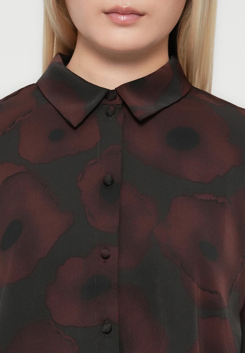 Zwarte shirt met bordeauxrood bloemenpatroon, voorzien van een puntige kraag en knoopsluiting, gemaakt van een zachte, lichte stof.