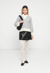 Jonge vrouw in een wit en blauw geblokt trui, zwarte leren rok, witte panty, donkerrode ballerina's en met een zwarte schoudertas.