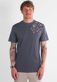 T-shirt à manches courtes, gris foncé, en coton, avec une broderie florale rose et blanche sur l'épaule gauche et la partie supérieure de la poitrine.