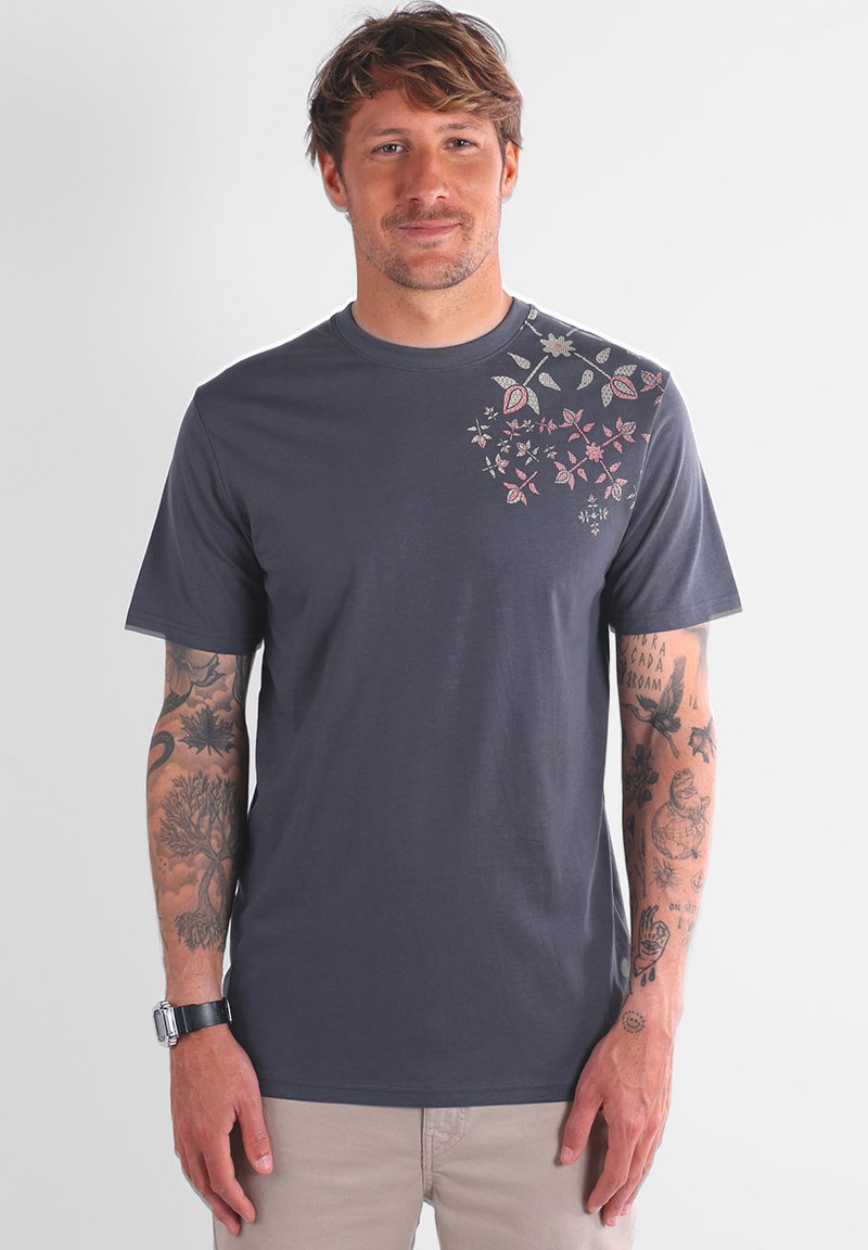 T-shirt à manches courtes, gris foncé, en coton, avec une broderie florale rose et blanche sur l'épaule gauche et la partie supérieure de la poitrine.
