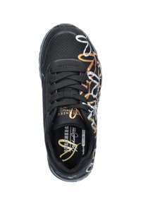 Zapatilla negra con parte superior lisa y perforaciones, acentos decorativos de estilo graffiti en blanco y naranja, suela flexible y cierre de cordones.