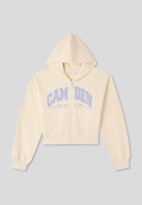 Felpa cropped con zip di un leggero color crema, dotata di cappuccio con cordoncino. Presenta testo blu: "CAMDEN" e "STAY TRUE DREAMS ALWAYS." Tessuto morbido.