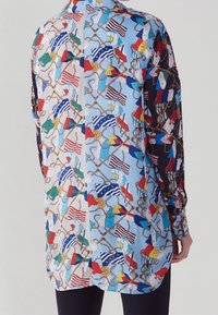 Langsleeve shirt met een meerkleurige maritieme vlaggenprint op een lichtblauwe achtergrond, met een zwarte zijkant en een soepele stoftextuur.