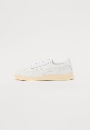 Baskets blanches basses avec des détails perforés, des lacets blancs et une semelle beige, présentées de profil sur un fond uni.