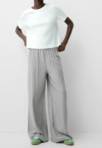 Vit kortärmad topp, grå randiga vida byxor och gröna skor. Byxorna har en avslappnad passform och midjeband med elastisk resår.