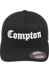 Čierna baseballová šiltovka s zahnutým šiltom a bielym vyšitým textom "Compton" v štýlovom písmene. Štítok uvádza veľkosť Flexfit S/M.