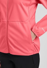 Giacca softshell rosa con zip completa, tasche laterali e polsini elasticizzati, realizzata in tessuto testurizzato e traspirante.