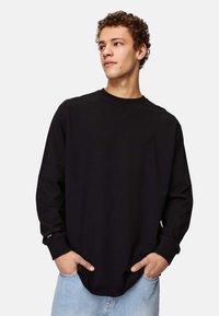 Black long-sleeve shirt with crew neck. Features a small embossed logo on the chest, made from a smooth cotton material.