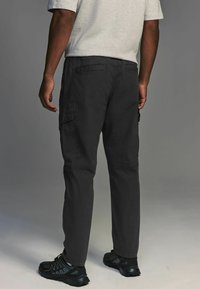 Pantaloni cargo gri închis, fabricați dintr-un material durabil, cu buzunare laterale, o croială lejeră și manșete elastice la glezne. Pantofi sport negri.