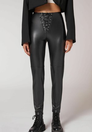 Hoch-taillierte schwarze Leggings aus Kunstleder mit einer Schnürung an der Vorderseite, glatter Textur und enganliegendem Design, mit schwarzen Nähten und Akzenten.