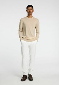 Μπεζ ζακέτα με μακριά μανίκια, λευκά παντελόνια και καφέ υποδήματα. Το outfit διαθέτει στενή γραμμή με μαλακό ύφασμα και στρογγυλή λαιμόκοψη.