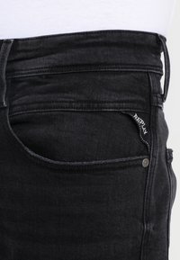 Svarta denimjeans med smal passform. Funktioner inkluderar en främre ficka, synlig sömnad och en vävd varumärkesetikett på fickan.