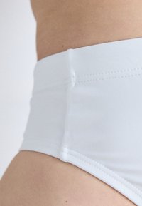 Vit högmidjad bikiniunderdel gjord av texturerat tyg med synlig sömnad. Har en mjuk yta och en åtsittande passform runt midjan.