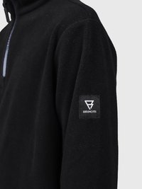 Giacca in pile nera con zip a quarto e un'etichetta quadrata con il logo "Brunotti" sulla manica superiore, su uno sfondo neutro.
