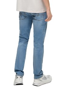 Jasnoniebieskie dżinsy o prostym kroju, z pięcioma kieszeniami i subtelnymi detalami przeszycia, w połączeniu z białymi sportowymi trampkami.