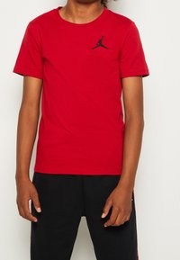 Červené bavlněné tričko s krátkým ruk�ávem, na hrudi s černě vyšívaným logem Jordan. Jednoduchý design s kruhovým výstřihem, hladká textura.