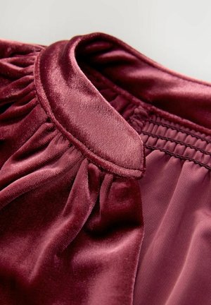 Burgundi szatén anyag redőzött gallérral és elasztikus ráncolás részlettel. Puha, sima textúra enyhe fényes felülettel és tiszta szegélyekkel.