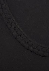 Svart tyg med en slät textur, med en flätad design längs halslinningen för ytterligare detaljer.