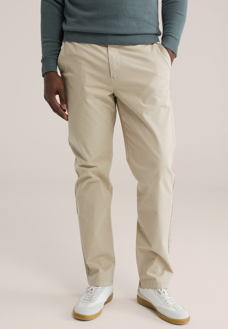 Pantalon beige en coton avec poches latérales, coupe décontractée et texture subtile. Assorti à des baskets blanches avec semelles en gomme.