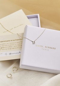 Collier en or avec un pendentif "B" sur une chaîne délicate, emballé dans une boîte blanche avec une inscription dorée. Inclut un certificat d'authenticité.