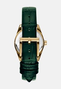 Horloge met een goudkleurige kast en een groene krokodillenleren band. De band heeft een glanzende afwerking en een tangsluiting. Zilveren achterkant zichtbaar.