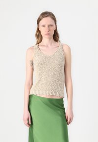 Beżowy dzianinowy top bez rękawów o teksturowanym wykończeniu i okrągłym dekolcie, zestawiony z zieloną satynową spódnicą. Prosty i nowoczesny design.
