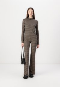 Houndstooth-patroon in bruin en beige, bestaande uit een fitted coltrui en flared broeken, aangevuld met zwarte schoenen en een tas.