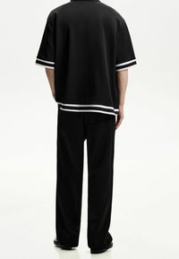 Musta lyhythihainen poolopaita, jonka hihansuuissa ja helmassa on valkoiset kaksinkertaiset raidat, yhdistetty mustiin leveälahkeisiin housuihin. Kangas vaikuttaa sileältä ja joustavalta.