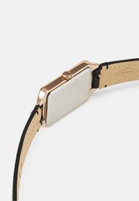 Roségold rechteckige Uhr mit glattem Edelstahlgehäuse, schwarzem Lederarmband und strukturiertem beigen Unterseite. Runde Krone ist sichtbar.