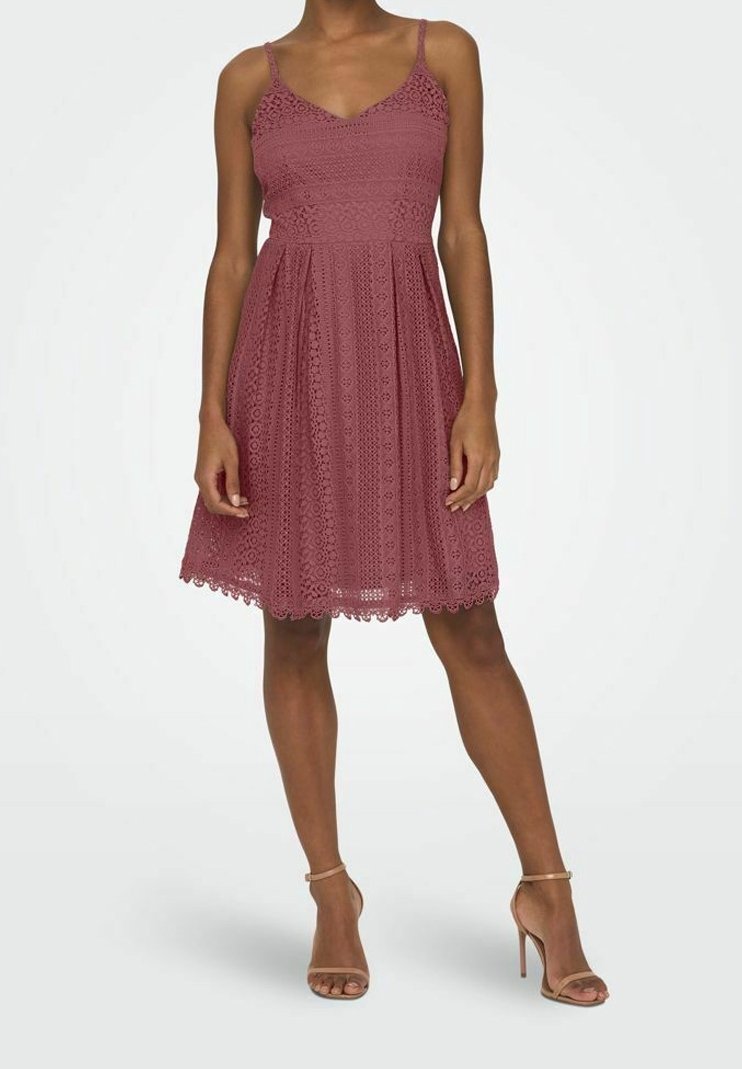 Robe en dentelle rose poudré avec un corsage ajusté et une jupe évasée. Elle présente des bretelles fines et un ourlet festonné.