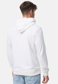 Hvid hættetrøje lavet af blødt stof, med snoretræk i hætten, ribbet manchetter og kant, med et enkelt design og ingen synlige logoer.