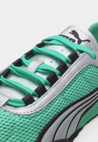 Κοντινή λήψη ενός αθλητικού παπουτσιού Puma σε πετρόλ και λευκό χρώμα με μαύρες λεπτομέρειες, κατασκευασμένο από διχτυωτό υλικό και ελαστικά κορδόνια σε πετρόλ που στερεώνονται με μαύρους κρίκους κορδονιών.