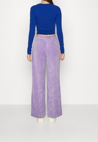 Långärmad blå topp som är parat med vida ljuslila kordbyxor med texturerad yta och bakfickor.