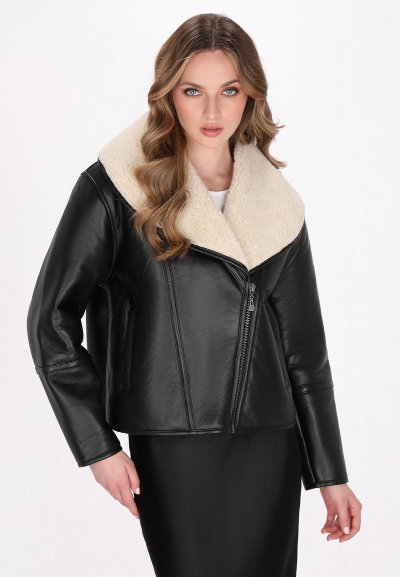 Schwarze Lederjacke mit einem breiten Kragen aus cremefarbenem Kunstfell, Reißverschluss und seitlichen Taschen. Glatte Textur und kurzes Design.
