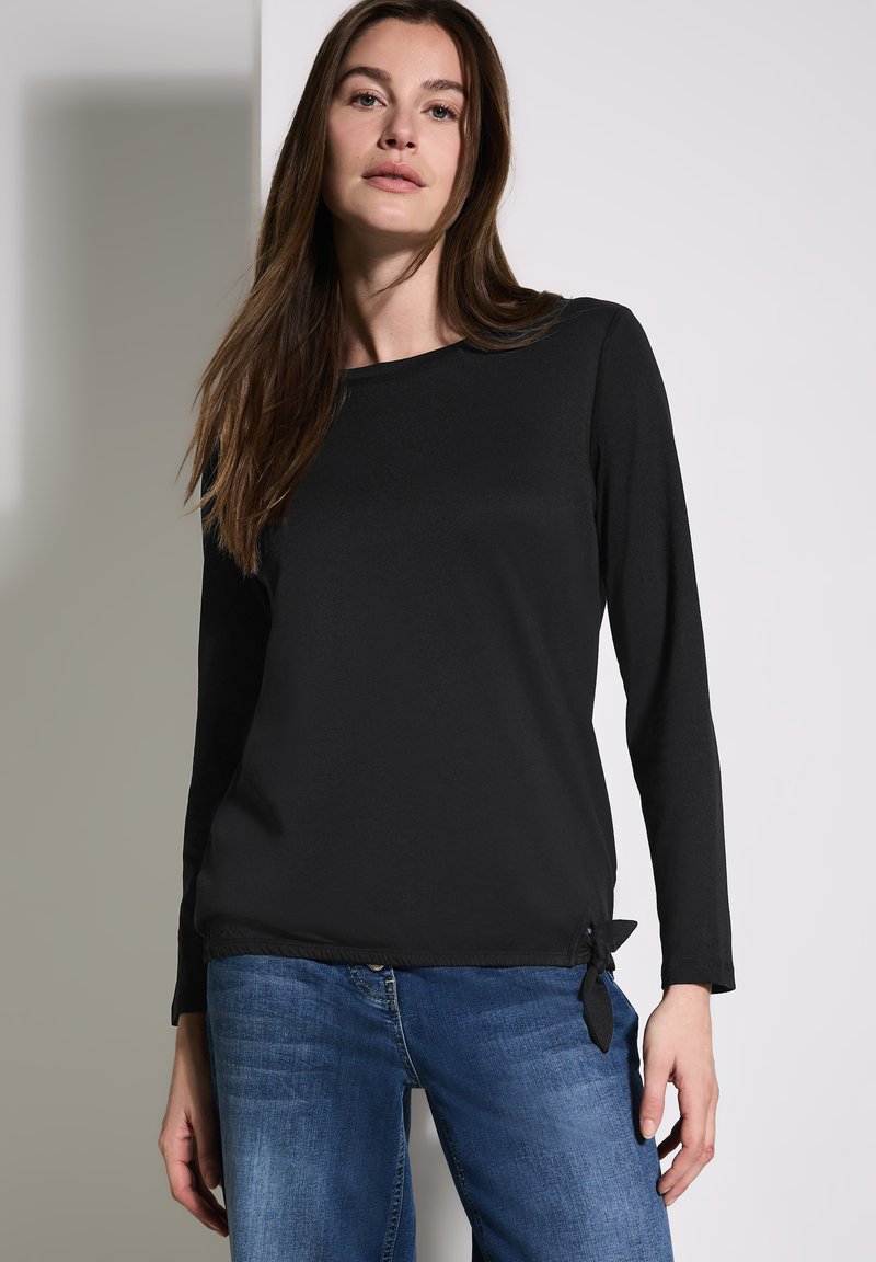 Maglietta nera a maniche lunghe con scollatura rotonda, in tessuto morbido, e un dettaglio a nodo sull'orlo inferiore, abbinata a jeans blu.