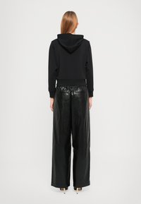 Zwarte cropped hoodie met capuchon en geribbelde zoom, gecombineerd met hooggetailleerde, wijde zwarte leren broek met een elastische tailleband.