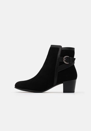 Boot en daim noir à talon bloc avec une lanière latérale munie d'une boucle ronde argentée, présenté sur fond blanc.