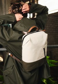 Zaino con una parte superiore bianca, parte inferiore verde scuro e dettagli in pelle. Presenta spallacci regolabili e una cerniera per una chiusura sicura.