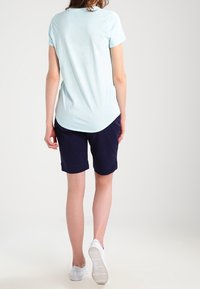 T-shirt bleu clair à manches courtes avec un ourlet arrondi, associé à un short bleu marine. Baskets blanches visibles, texture lisse, coupe décontractée.