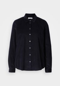 Chemise noire à manches longues avec col pointu, sept boutons sur le devant et une étiquette Marc O'Polo à l'intérieur du col.