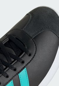 Sort sneakers med en glat læderfinish, turkise striber, strukturerede ruskindselementer og sorte snørebånd. Hvid gummisål synlig.