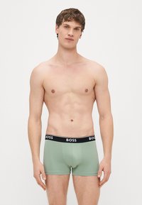Cuecas boxer verdes em algodão com cintura preta e o logótipo branco "BOSS". Textura suave e design ajustado.