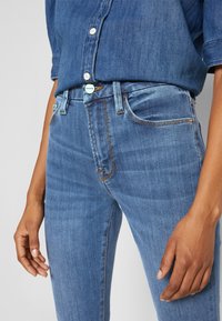 Vaqueros de mezclilla azules con un diseño ajustado, cinco bolsillos, costuras en contraste y una superficie texturizada. Acompañados de una camisa azul a juego.