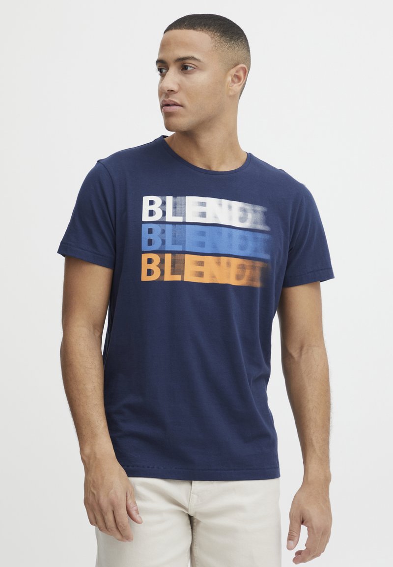 Tamsiai mėlynos medvilnės marškinėliai su grafiniu dizainu, kuriame žodis "BLEND" pateikiamas skirtingomis baltos, mėlynos ir oranžinės spalvomis. Trumpomis rankovėmis, apvaliu iškirpimu.