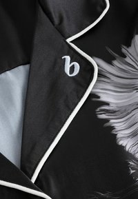 Taflă de satin neagră cu piping alb, având un model floral în nuanțe de gri. Logo-ul brodat 'b' pe guler. Textură netedă.